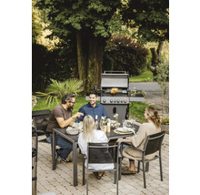 Scène extérieure avec un barbecue à gaz, une table à manger et quatre personnes en train de manger.