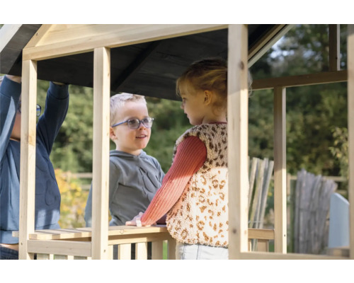 Zwei Kinder spielen in einem unbehandelten Holzspielhaus im Garten.