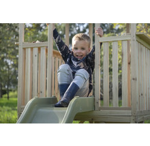 Un enfant est assis sur un toboggan en bois avec une rampe dans une aire de jeux