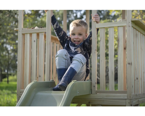 Un enfant est assis sur un toboggan en bois avec une rampe dans une aire de jeux