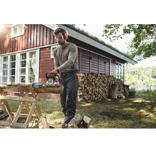Mann sägt Holz mit einer Kettensäge im Garten, Schutzbrille, Gehörschutz