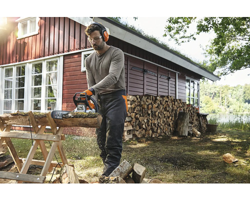 Mann sägt Holz mit einer Kettensäge im Garten, Schutzbrille, Gehörschutz