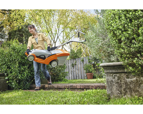 Une femme porte une tondeuse à gazon dans un jardin.