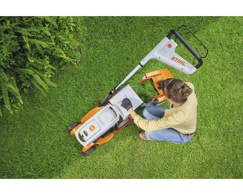 Vue de dessus d'une femme préparant une tondeuse à gazon sur une pelouse. Logo Stihl.