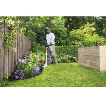 Jardinier coupant les bordures de pelouse avec un coupe-bordure dans un jardin avec une clôture en bois et un parterre surélevé