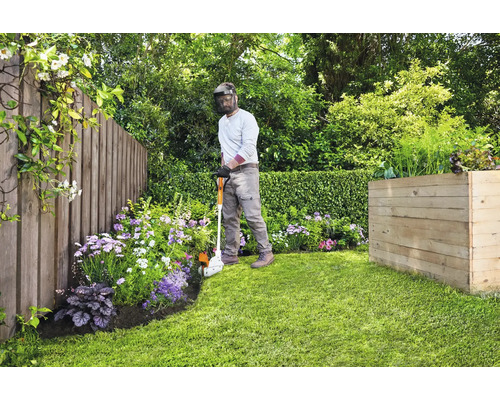 Jardinier coupant les bordures de pelouse avec un coupe-bordure dans un jardin avec une clôture en bois et un parterre surélevé