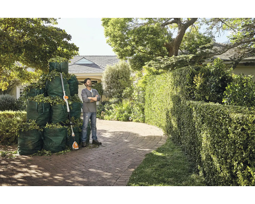 Un homme se tient à côté d'un taille-haie et de sacs de jardin remplis devant une maison.