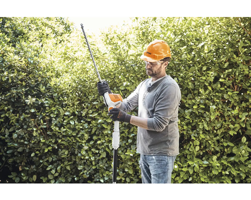 Homme portant un casque et des lunettes de protection taillant une haie avec un taille-haie.