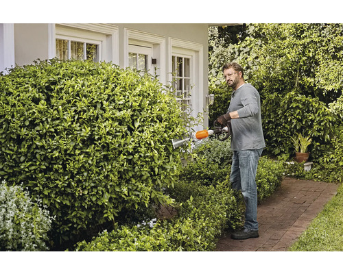 Un homme taille une haie avec un taille-haie dans un jardin.