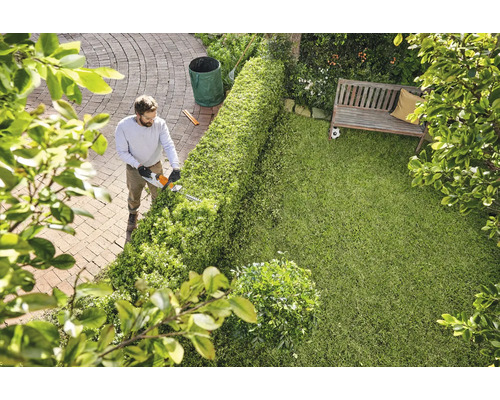 Un homme taille une haie avec un taille-haie dans un jardin.