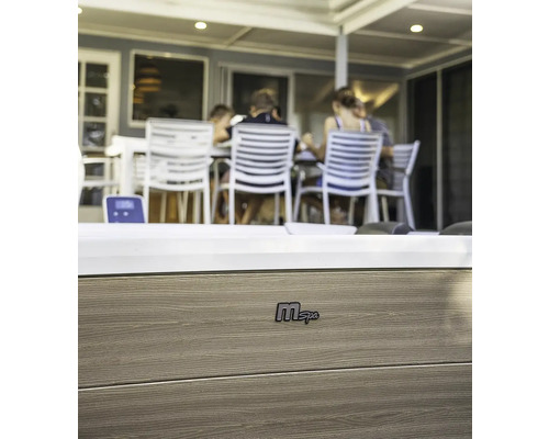 Gros plan d''un jacuzzi MSpa avec revêtement en bois et le logo MSpa. À l''arrière-plan, des personnes sont assises à une table.