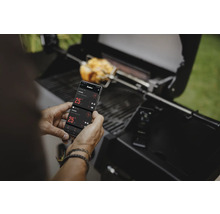 Un homme utilise une application smartphone pour contrôler son barbecue pendant que le poulet grille
