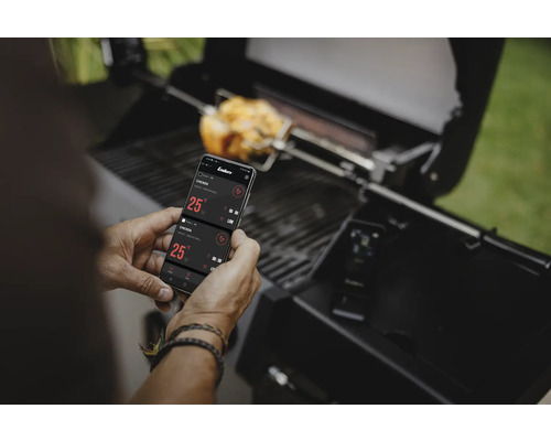 Un homme utilise une application smartphone pour contrôler son barbecue pendant que le poulet grille