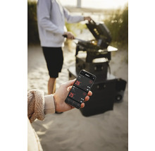 Une personne fait des grillades avec un gril et contrôle la température avec une application sur un smartphone.