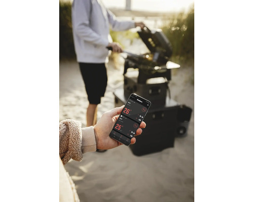 Une personne fait des grillades avec un gril et contrôle la température avec une application sur un smartphone.