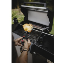 Homme utilisant une application smartphone pour contrôler le barbecue, avec des aliments sur une broche