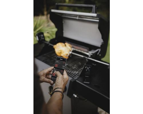 Homme utilisant une application smartphone pour contrôler le barbecue, avec des aliments sur une broche