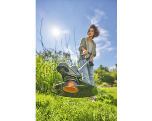 Une femme travaille avec un coupe-bordure dans le jardin.