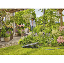 Garten mit Regner und einer Frau, die Pflanzen bewässert