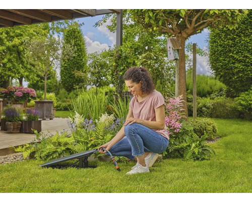 Une femme utilise un enrouleur de tuyau dans le jardin pour arroser les plantes.