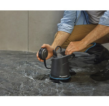 Un homme est accroupi sur le sol et actionne une pompe à eau sale Gardena dans l''eau.