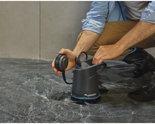 Un homme est accroupi sur le sol et actionne une pompe à eau sale Gardena dans l''eau.