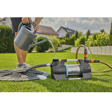 Une personne remplit une pompe de surpression domestique Gardena avec de l''eau d''un arrosoir dans le jardin.