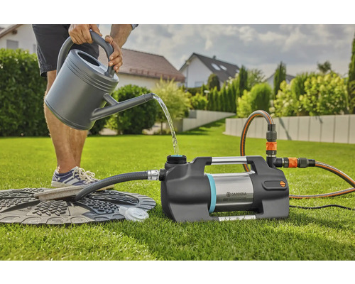 Une personne remplit une pompe de surpression domestique Gardena avec de l''eau d''un arrosoir dans le jardin.