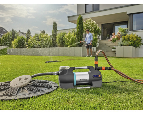 Scène d''irrigation de jardin avec pompe domestique, arroseur de pelouse et famille en arrière-plan