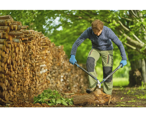 Mann spaltet Holz mit einer Astschere neben einem Holzstapel.