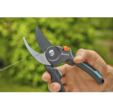 Une main tient un sécateur Gardena en train de couper une fine branche.