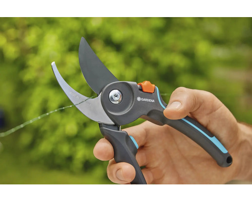 Une main tient un sécateur Gardena en train de couper une fine branche.