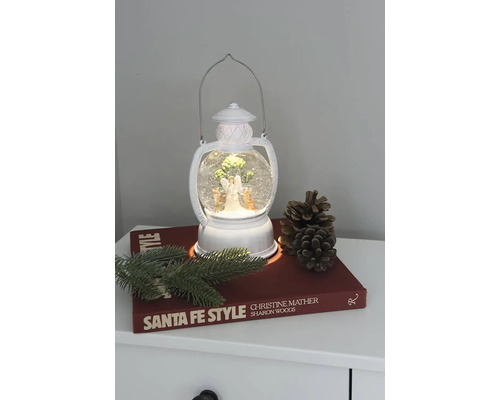 Lanterne décorative avec boule à neige, ange et sapin sur une table de chevet