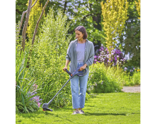 Femme coupant de l''herbe avec un coupe-bordure dans un jardin.