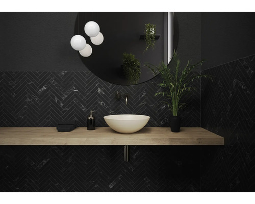 Salle de bain moderne avec lavabo, miroir, éclairage et carrelage foncé à chevrons.