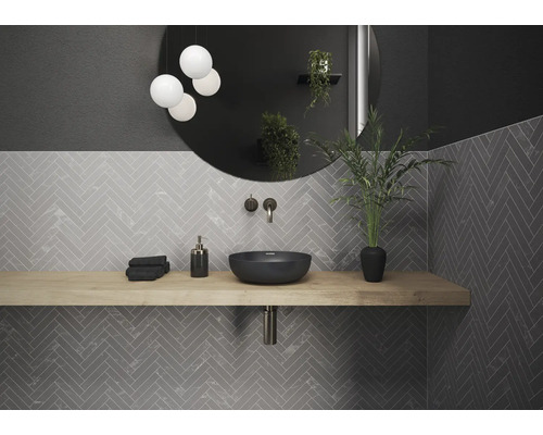 Salle de bain moderne avec lavabo, miroir, lampe et carreaux gris à chevrons.