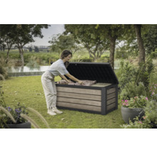 Szene im Garten mit einer Frau, die eine Gartenbox mit Holzoptik befüllt. Die Gartenbox steht auf einer Rasenfläche.