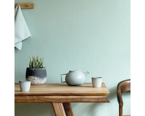Table en bois avec théière, tasses et plante en pot devant un mur