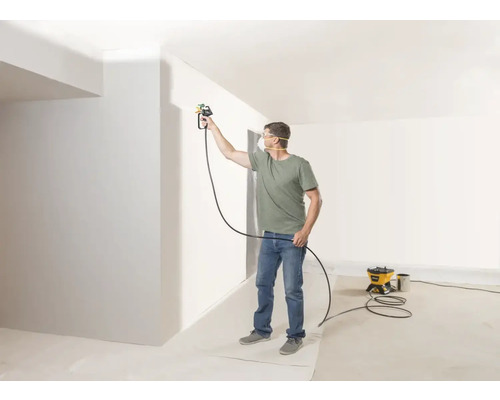 Un homme peint un mur avec un système de pulvérisation de peinture dans une pièce lumineuse