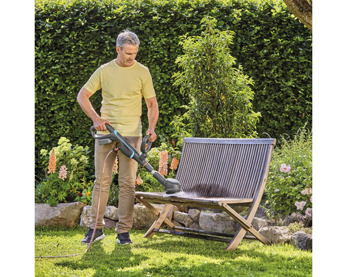 Homme nettoyant un banc en bois avec une brosse dans le jardin
