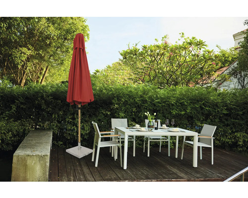 Scène de jardin avec parasol fermé, table de jardin et chaises de jardin sur une terrasse en bois devant une haie verte
