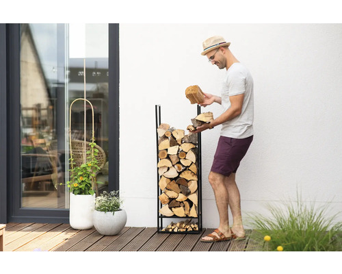 Mann befüllt ein Brennholzregal mit Holzscheiten im Garten