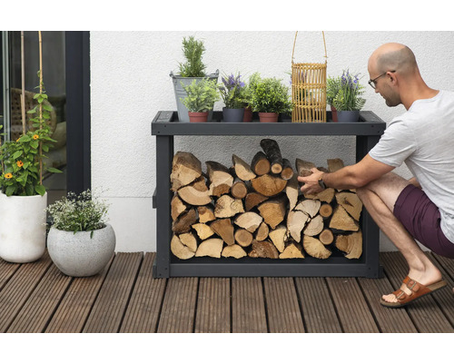 Holzregal mit Holz und Dekorationselementen im Außenbereich, eine Person befüllt das Regal