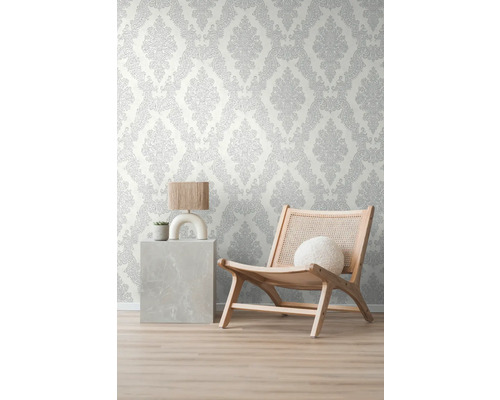 Raumansicht mit gemusterter Tapete, einem Sessel und einem Beistelltisch mit Lampe und Pflanze