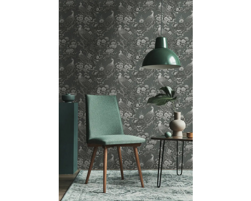 Wohnraumszene mit Tapete mit Pfauenmuster, Stuhl, Lampe und Beistelltisch