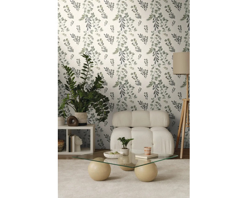 Wohnzimmer mit floral gemusterter Tapete, Sessel, Tisch und Zimmerpflanzen.