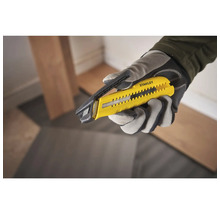 Eine Hand in einem Handschuh hält ein Stanley Teppichmesser.