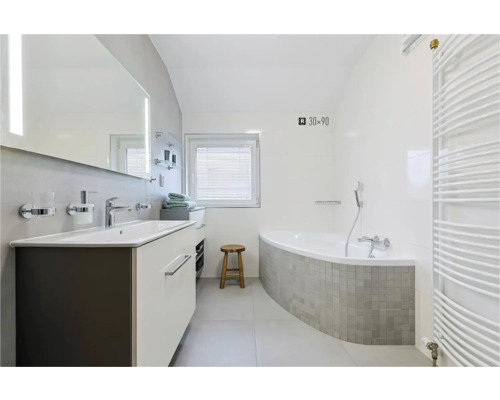 Badezimmer mit Waschtisch, Spiegel, Badewanne und Heizkörper