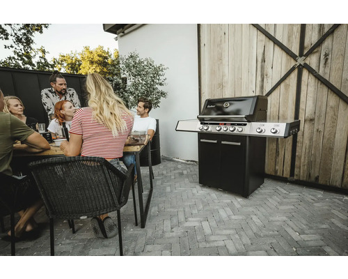 Szene im Freien mit einer Gruppe von Personen an einem Tisch und einem Enders Grill in der Nähe.