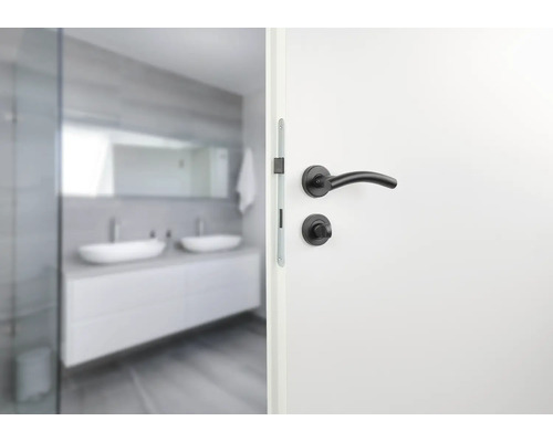 Weisse Tür mit schwarzem Türgriff und Badezimmer im Hintergrund